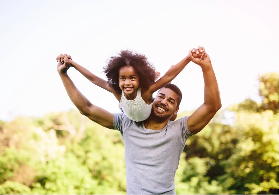A father lifting his smiling daughter on his shoulders outdoors
